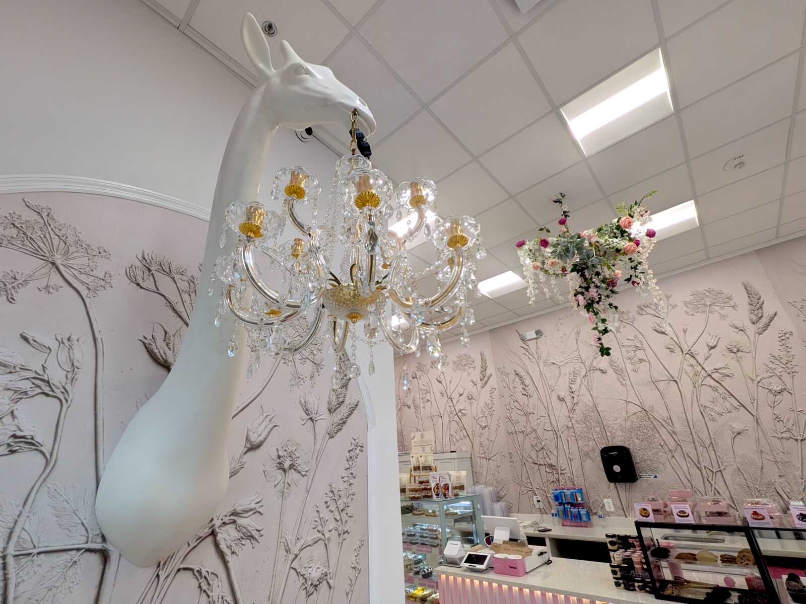 White giraffe sculpture supports a crystal chandelier in a pastel-themed boutique or bakery storefront display.