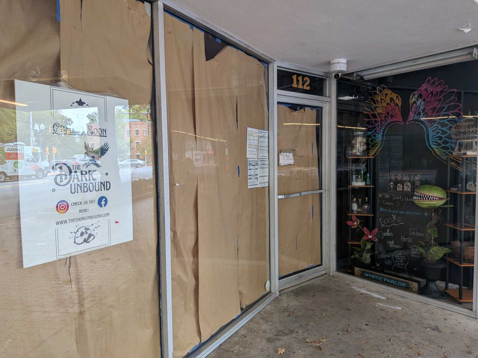 Closed storefront with windows covered in brown cardboard, door labeled 112, suggesting renovation or temporary closure.