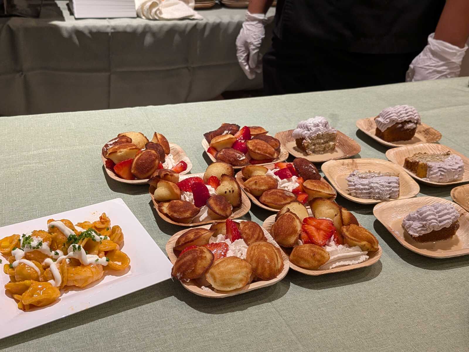 Assorted bite-size desserts (cream puffs, pastries, and strawberries) arranged on wooden plates on a pale green tablecloth.