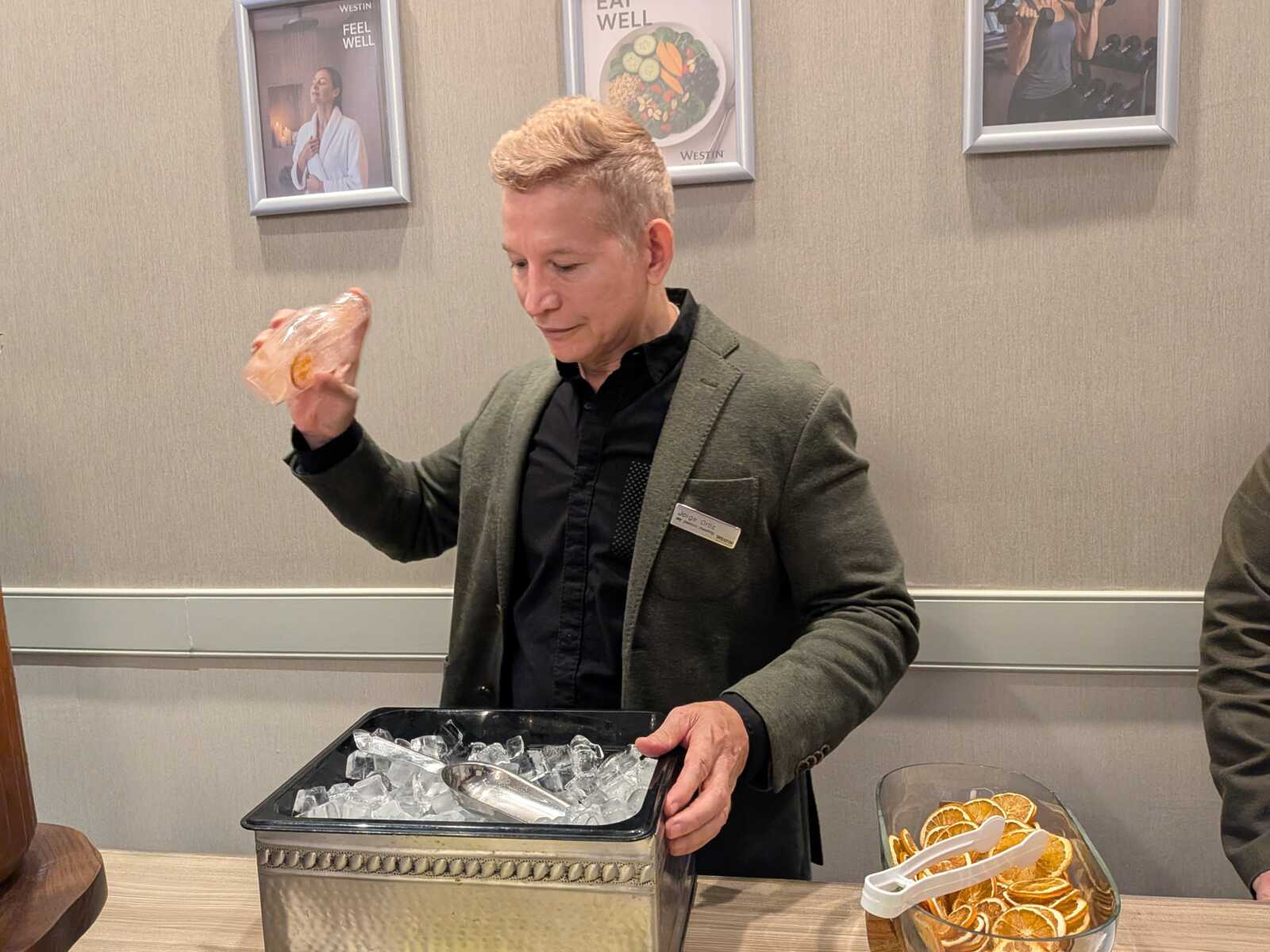 Man in a blazer with a name badge lifts a wrapped sandwich from a metal ice-filled bin at a buffet.