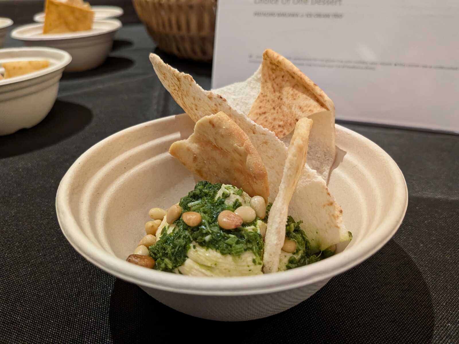 Bowl of greens (kale) dip topped with pine nuts and broken flatbread chips.
