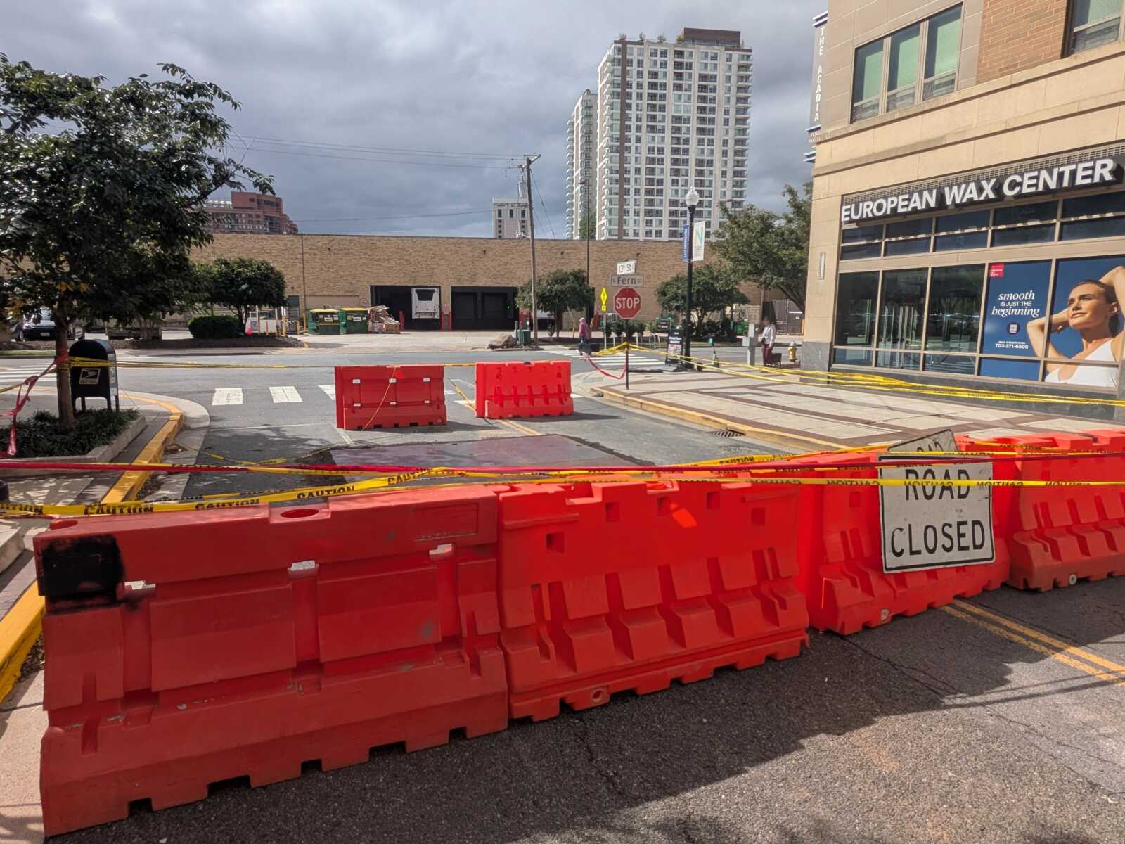 Street closed with orange barriers and caution tape; construction zone across a city street near a storefront.