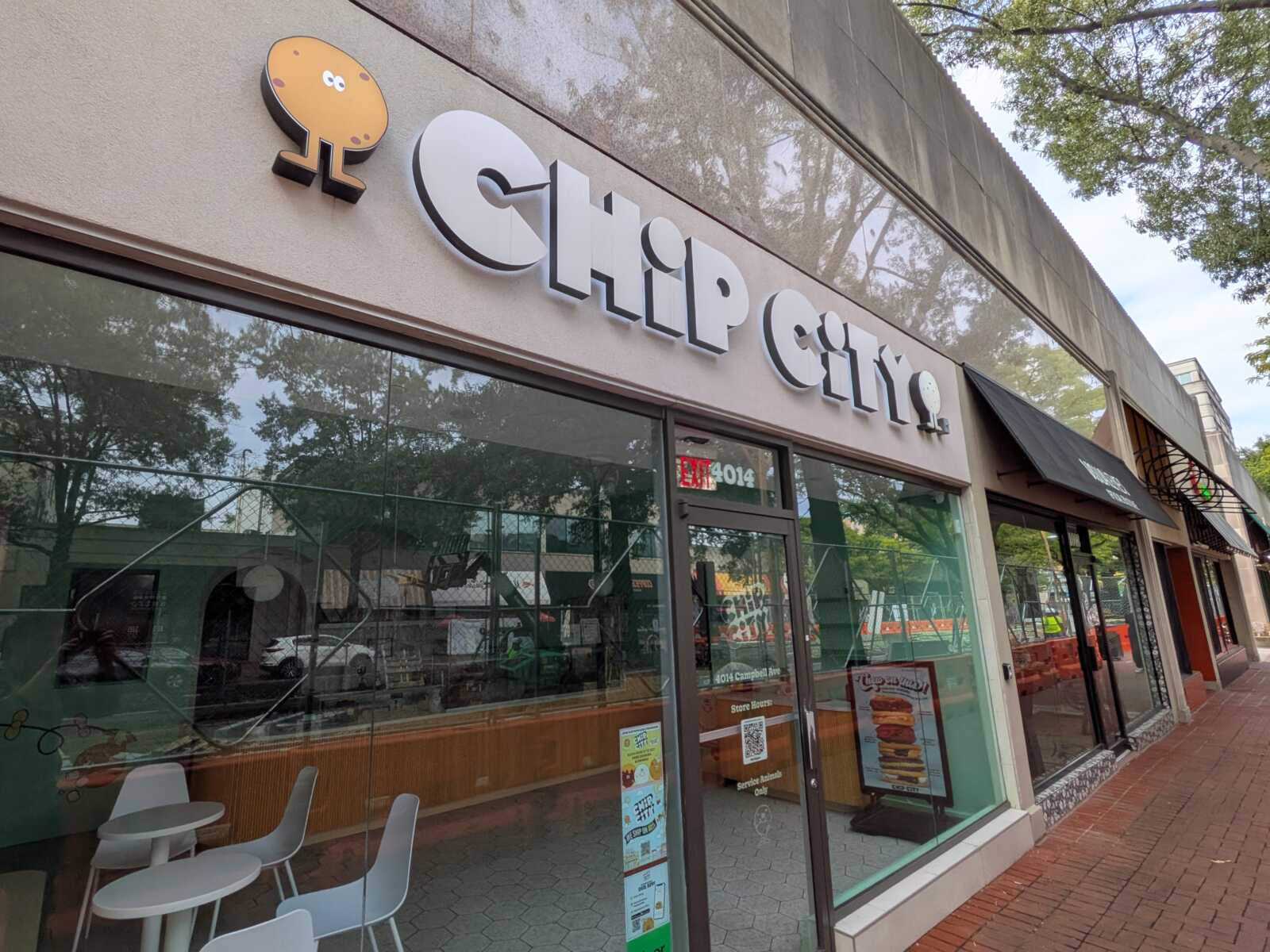 Chip City storefront with a cookie-shaped logo on a beige facade and glass windows reflecting trees.