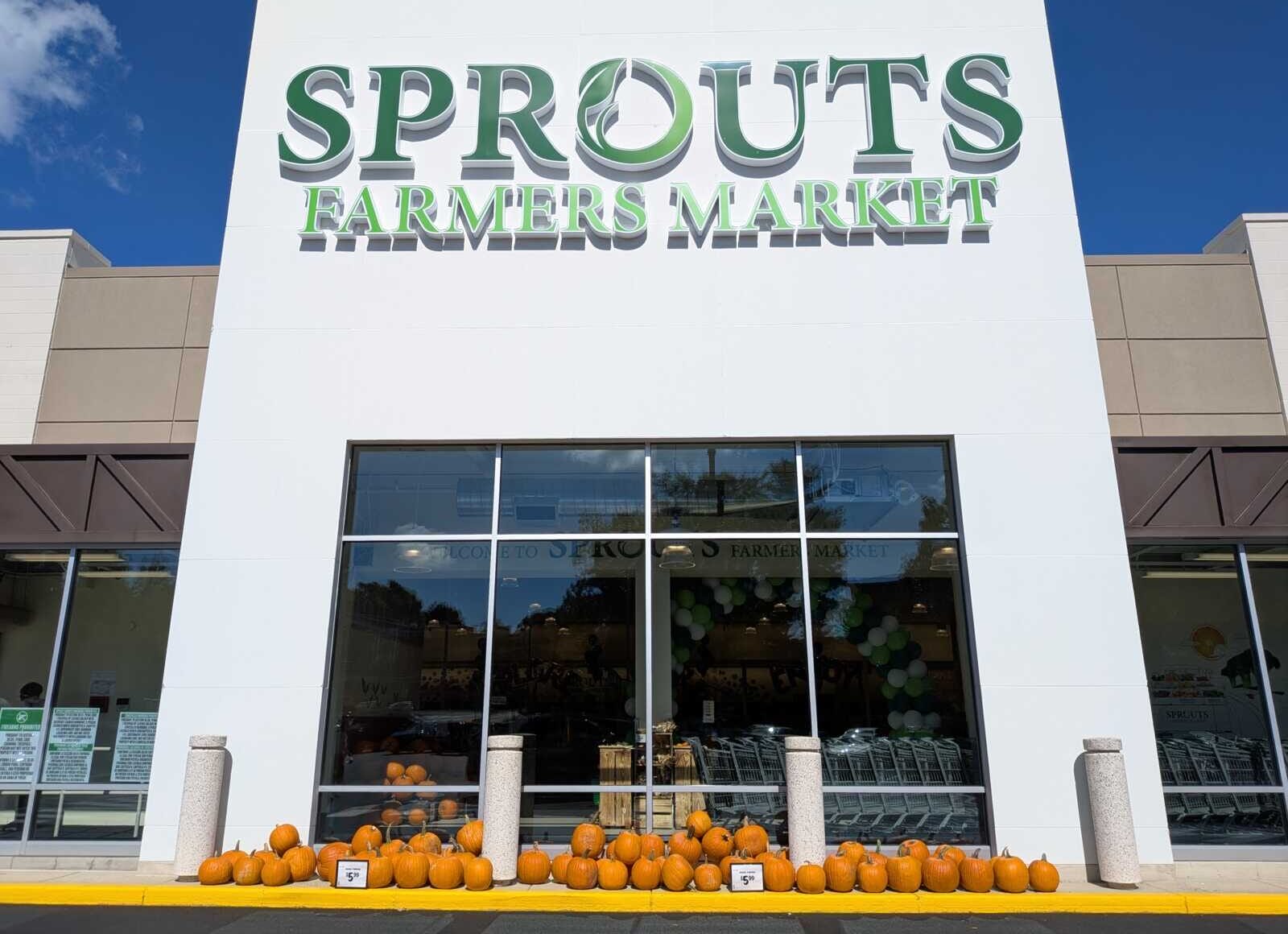 Facade of Sprouts Farmers Market with pumpkins lined along the storefront and blue sky above.