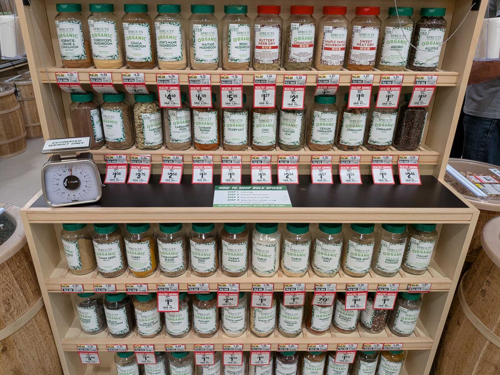 Display of many Sprouts Organic spice jars on wooden shelves in a grocery store.