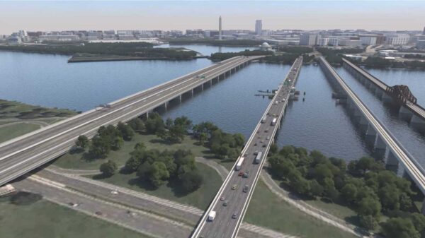 Aerial view of three elevated highways crossing a wide river with a city skyline in the distance.