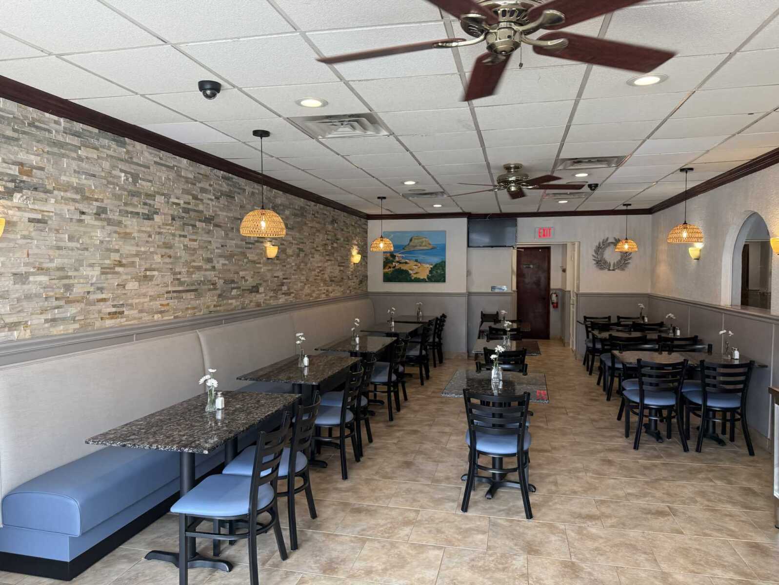 Cozy restaurant dining area with a stone accent wall, blue-cushioned booths, and small square tables with vases.