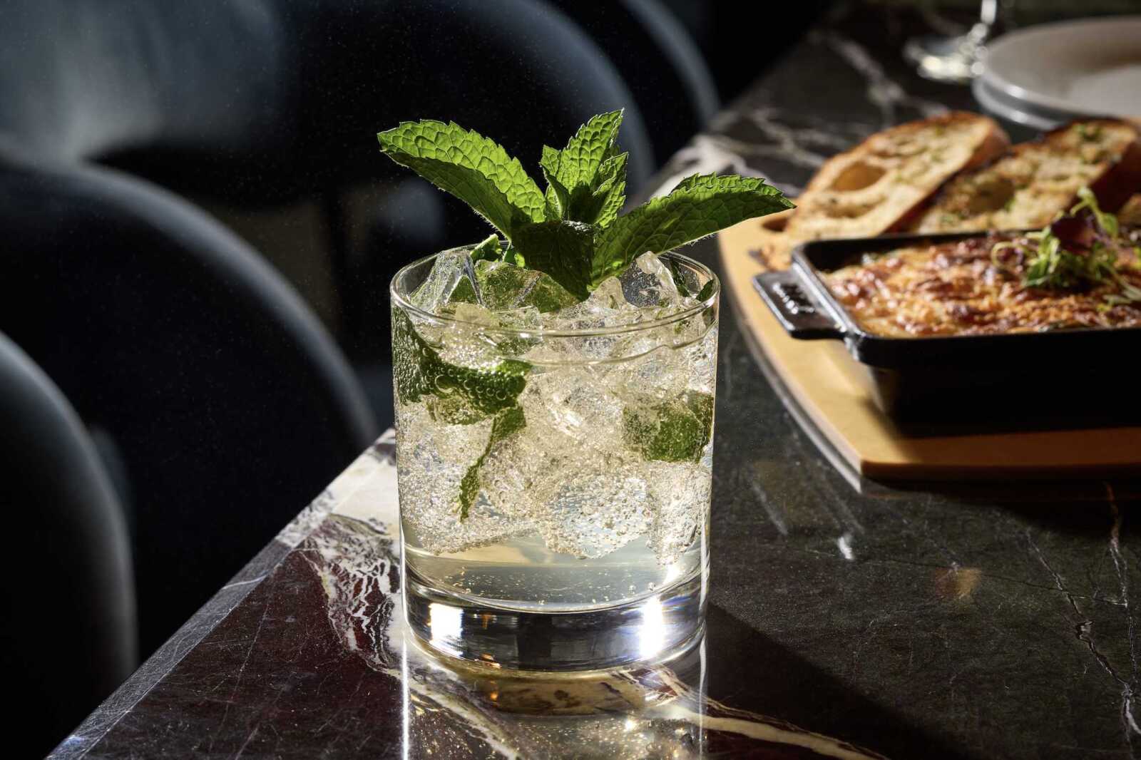 Highball glass filled with crushed ice and fresh mint leaves on a dark marble bar.