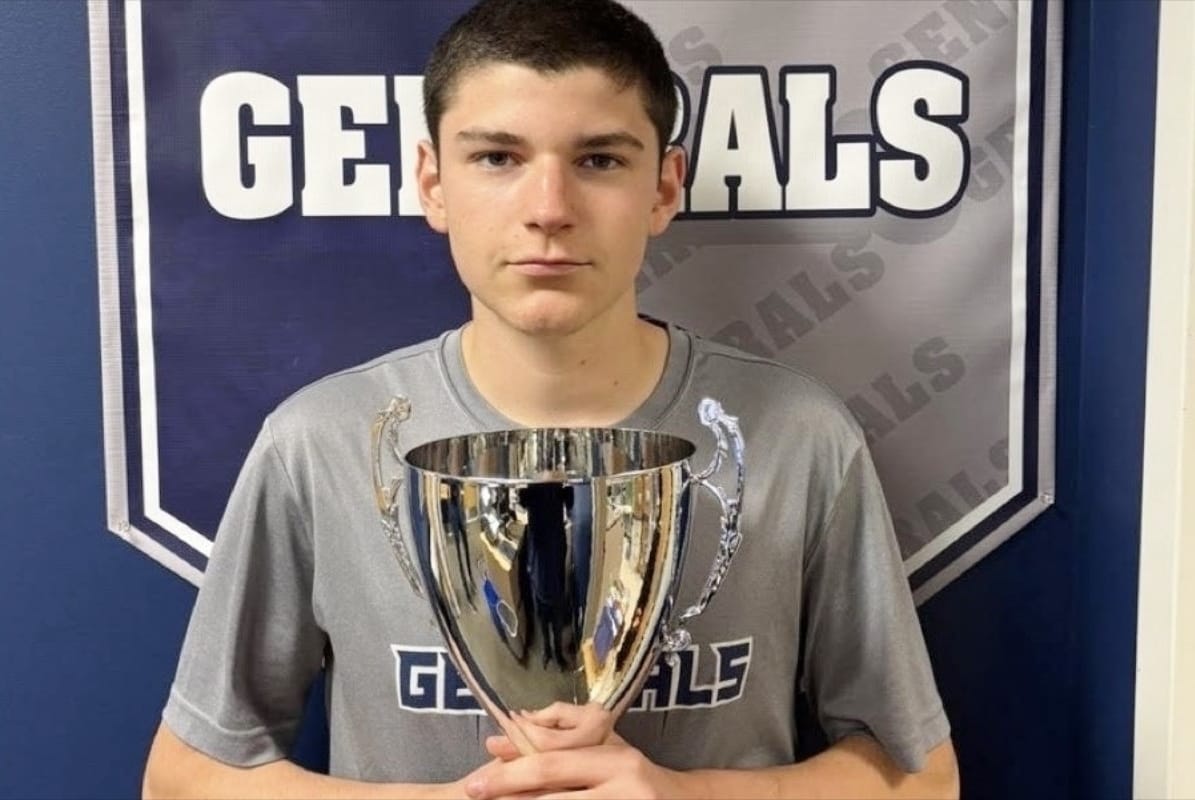Tyler Flint-Steinig displays his national trophy (photo from Washington-Liberty athletics) | ARLnow Young man in a gray t-shirt holding a large silver trophy in front of a Generals banner.