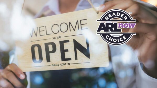 Wooden sign reading 'OPEN' with 'Welcome' and 'Please come in' held up to greet customers, with a circular 'Reader ARI Choice' logo overlay.