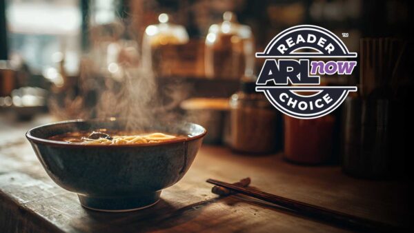 A steaming bowl of noodle soup on a wooden counter with chopsticks beside it and a bold circular logo reading 'Reader AR Now Choice' on the right.