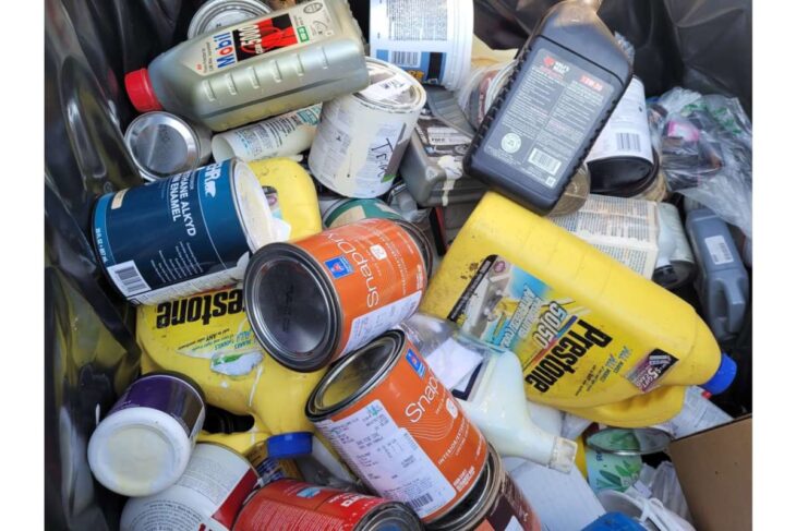 A messy trash bin filled with assorted paint cans, tins, and containers scattered inside.