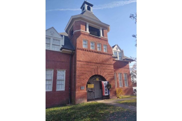 Red brick building with a small tower and arched entrance; a vertical OPEN banner hangs at the door.
