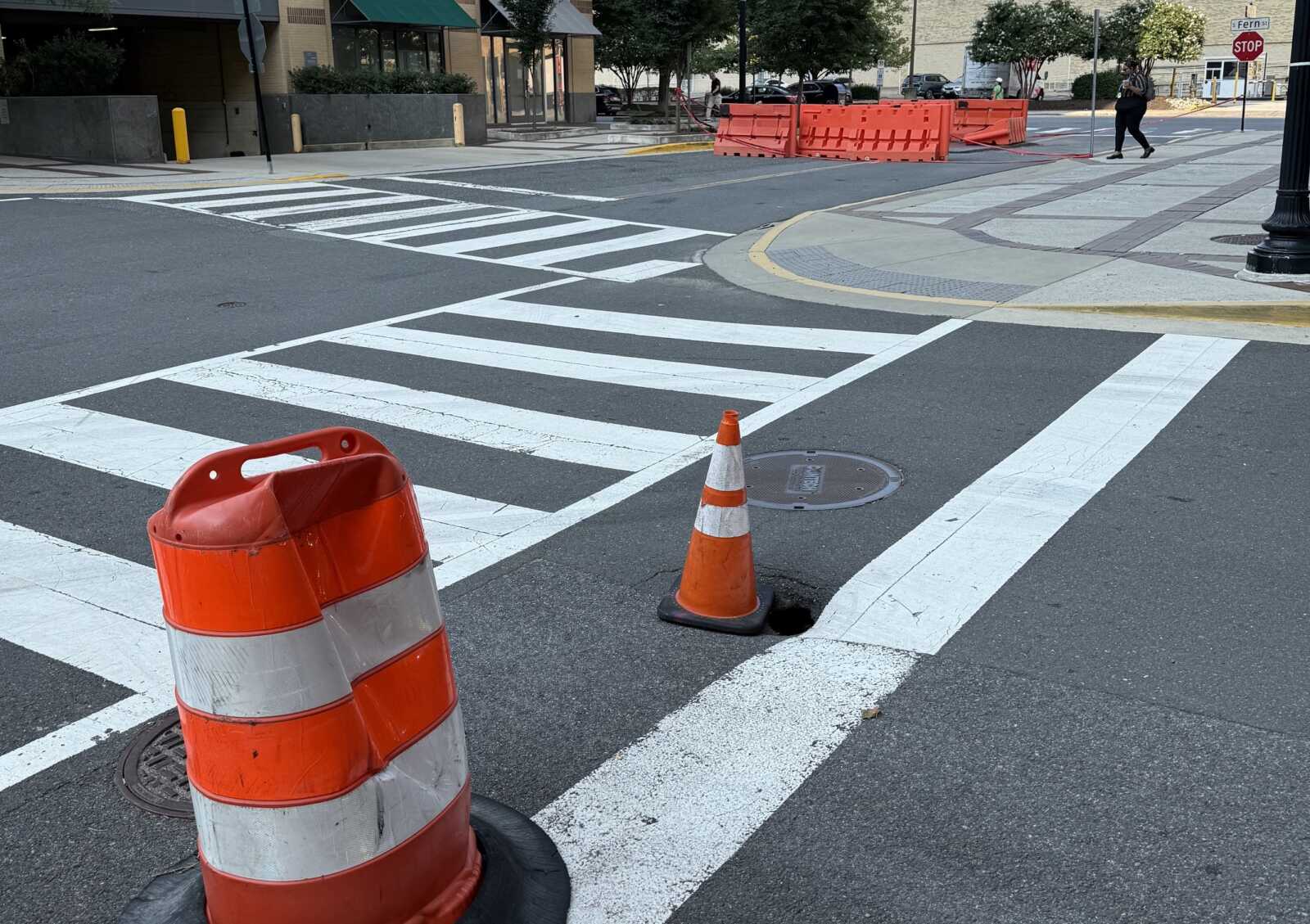 Crosswalk under construction with orange barriers and traffic cones on an urban street.