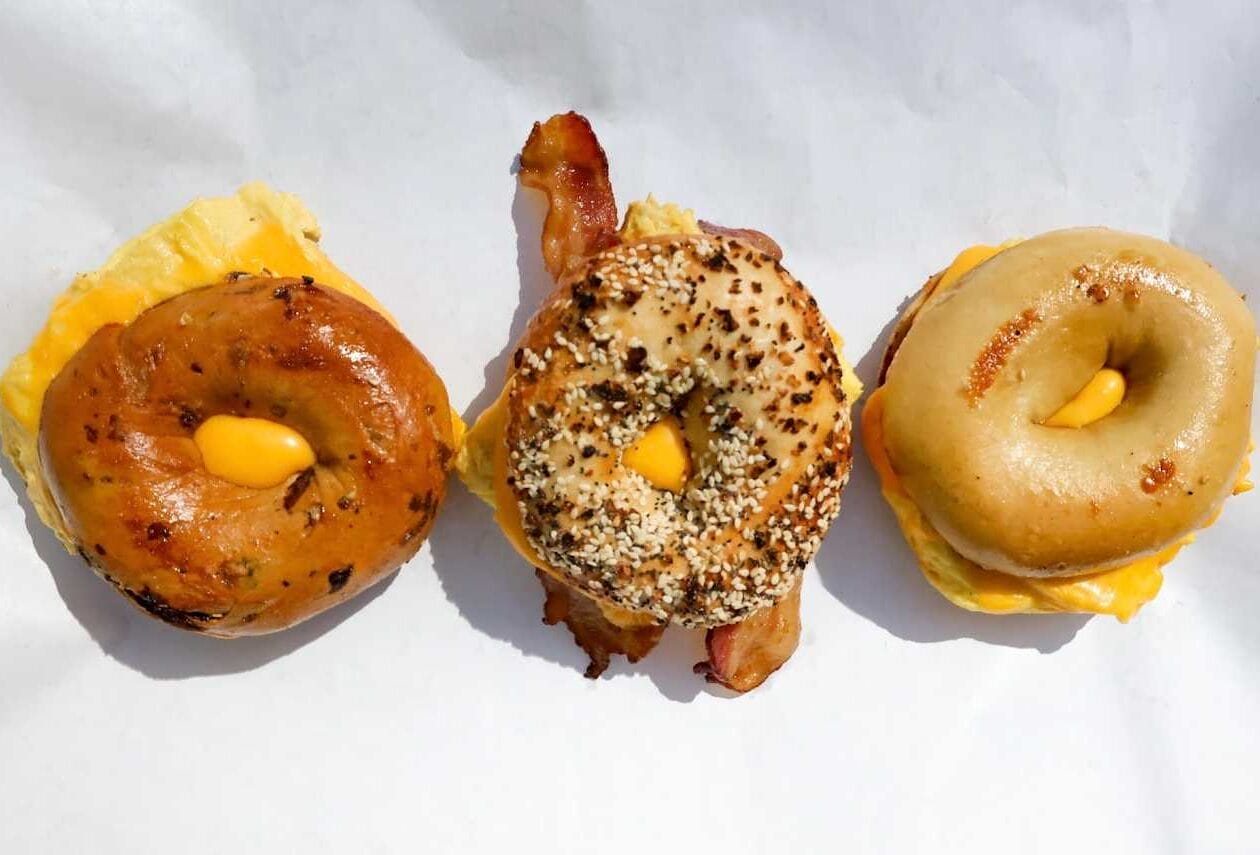Three breakfast sliders made with donut buns arranged in a row on white paper, each with melted cheese and egg.