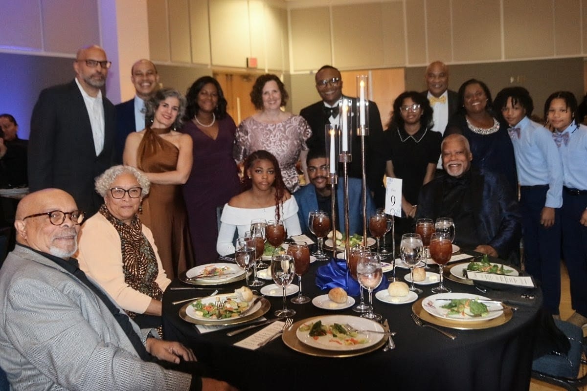 A diverse group of adults posing around a round dinner table at a formal event, smiling for the camera.