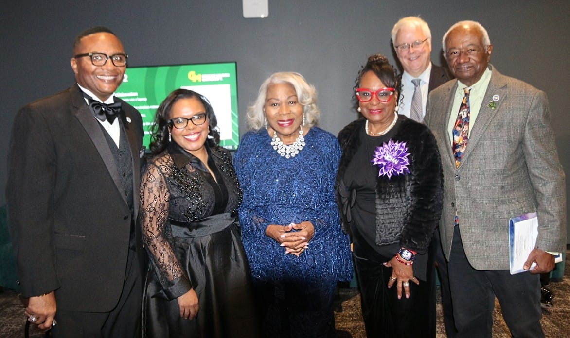 Group of six adults in formal attire posing for a photo at a formal event, smiling at the camera.