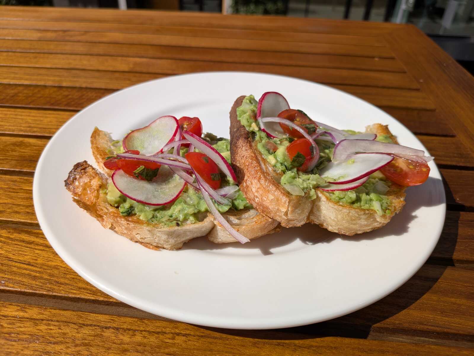 Plate of avocado toast topped with radish slices, cherry tomatoes, and red onion on crusty bread.