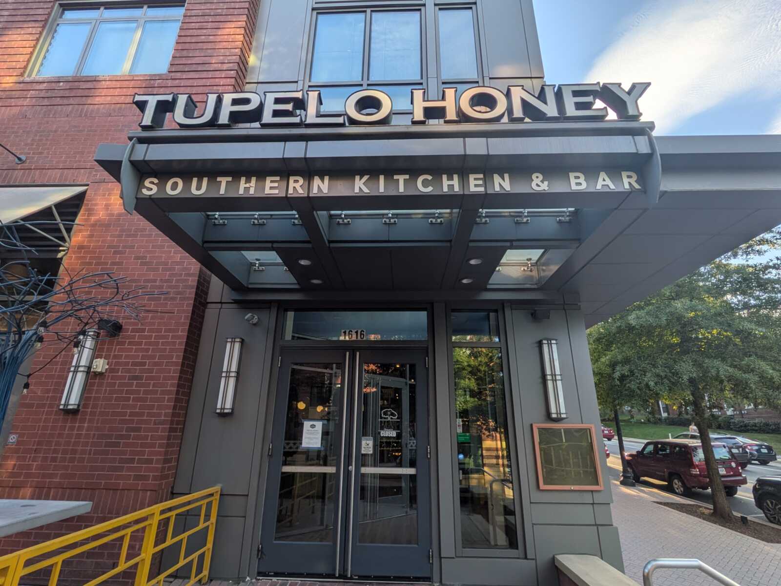 Entrance to Tupelo Honey restaurant, Southern Kitchen & Bar, with brick facade and glass doors under a gray canopy.