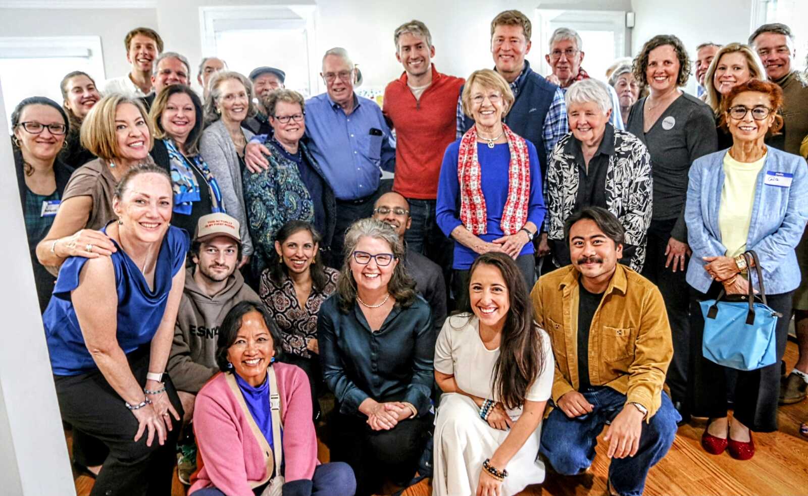 Diverse group of about 25 adults smiling in a bright room for a group photo.