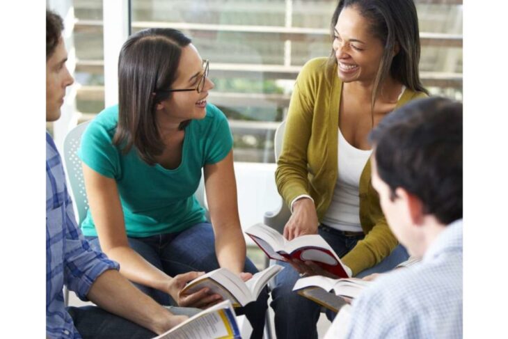 Four people seated in a circle, reading books and smiling during a study discussion.