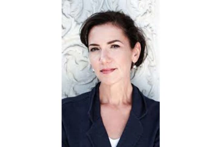 Professional portrait of a woman with short dark hair in a navy blazer against a carved white wall.