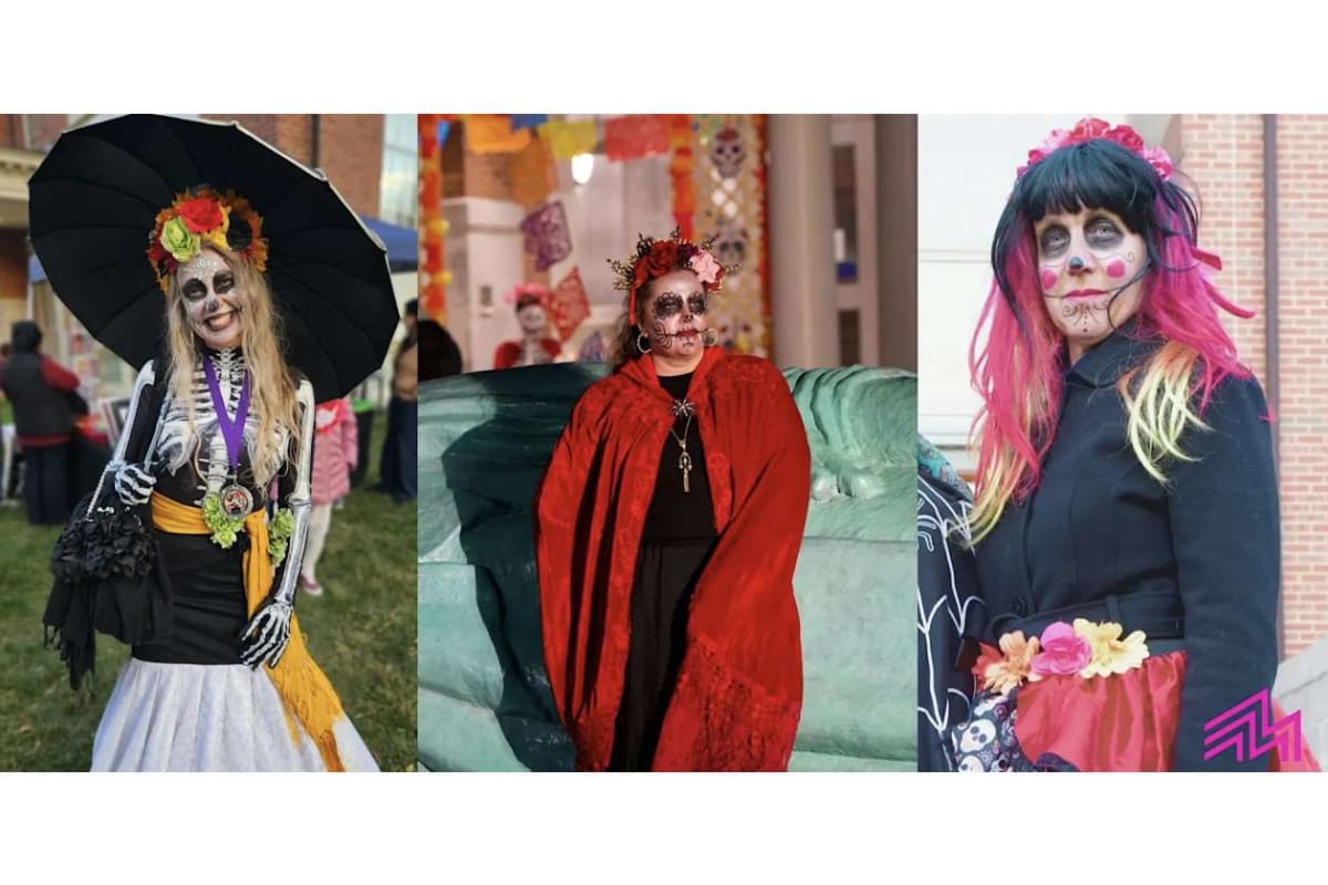 Three people in Day of the Dead costumes posing outdoors: left with black parasol and flower crown, middle in red cape, right with pink-bleached hair and skull makeup.