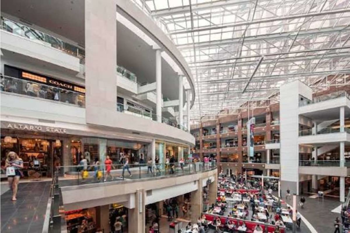 Interior view of a multi-level shopping mall with storefronts, glass railings, and a busy food court below.