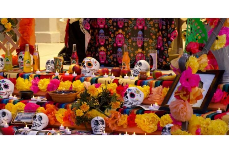 Dia de los Muertos altar with sugar skulls, candles, and bright marigold flowers on a colorful table.