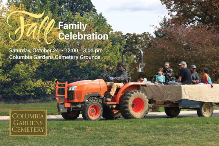 Fall Family Celebration at Columbia Gardens Cemetery Grounds with a orange tractor pulling a covered trailer, group of people aboard, autumn trees in background.
