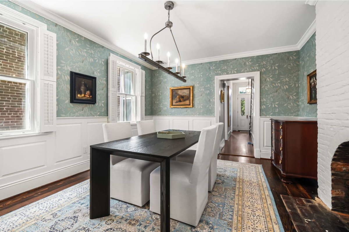 Dining room with a dark rectangular table and six white upholstered chairs, teal botanical wallpaper, and a hanging chandelier above the table
