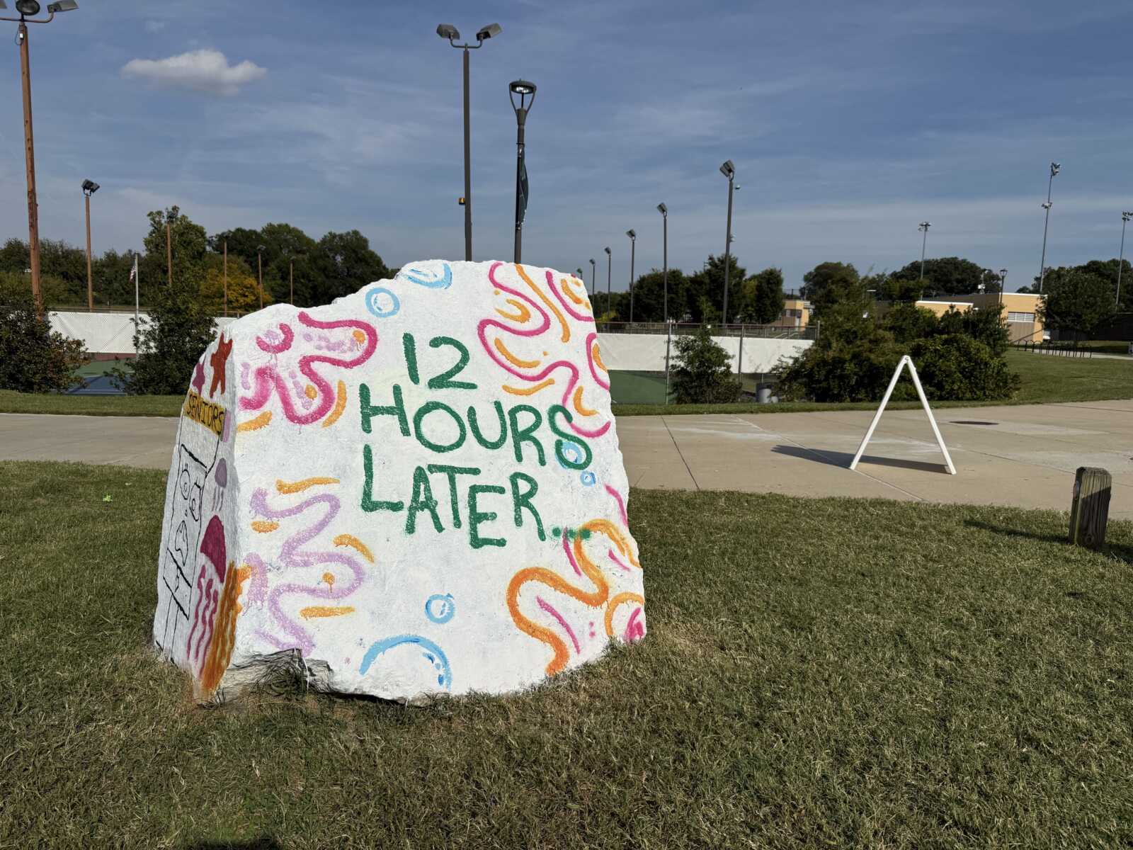 Large painted rock in a park reading '12 HOURS LATER...' with colorful swirls and patterns around the text